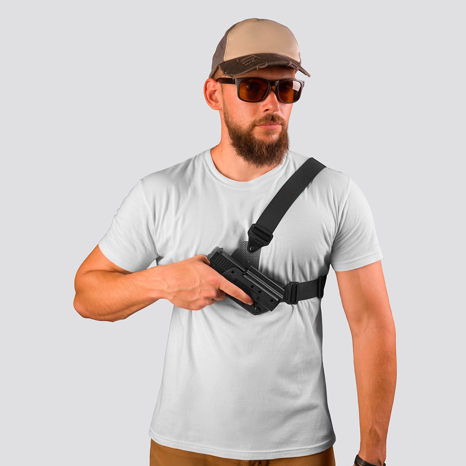 Man wearing a white t-shirt, beige cap, and sunglasses holding a black gun holster.