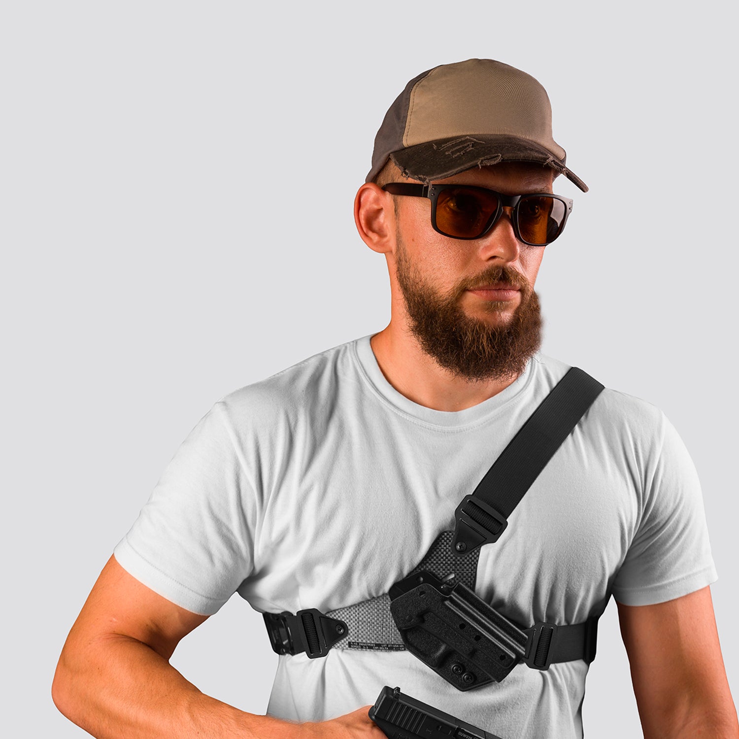 Man wearing a white t-shirt, brown cap, sunglasses, and carrying a black crossbody bag on a light gray background