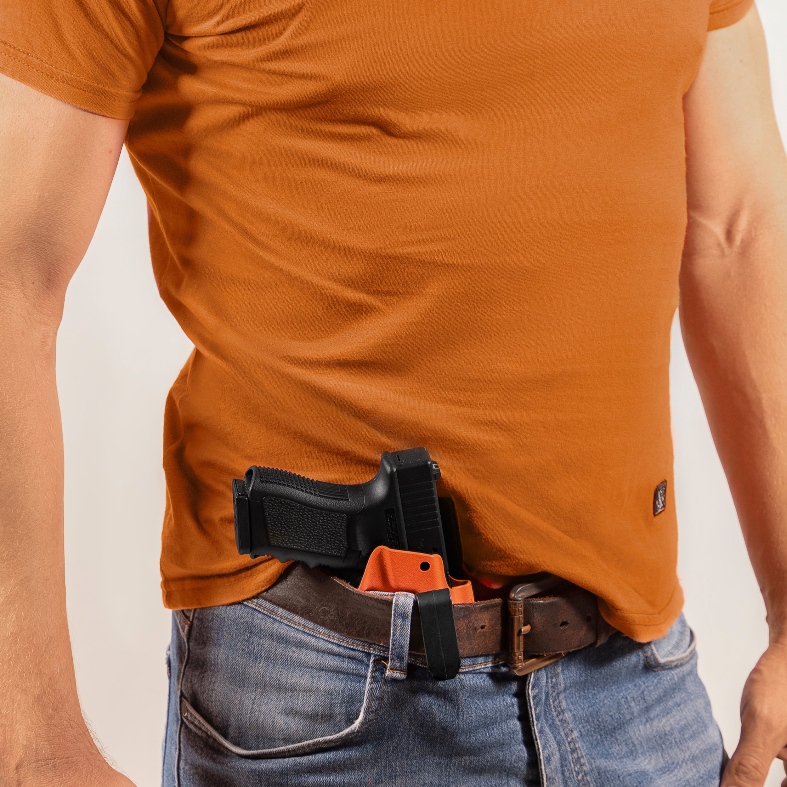 Person wearing a brown t-shirt with a black and orange holster on a plain background