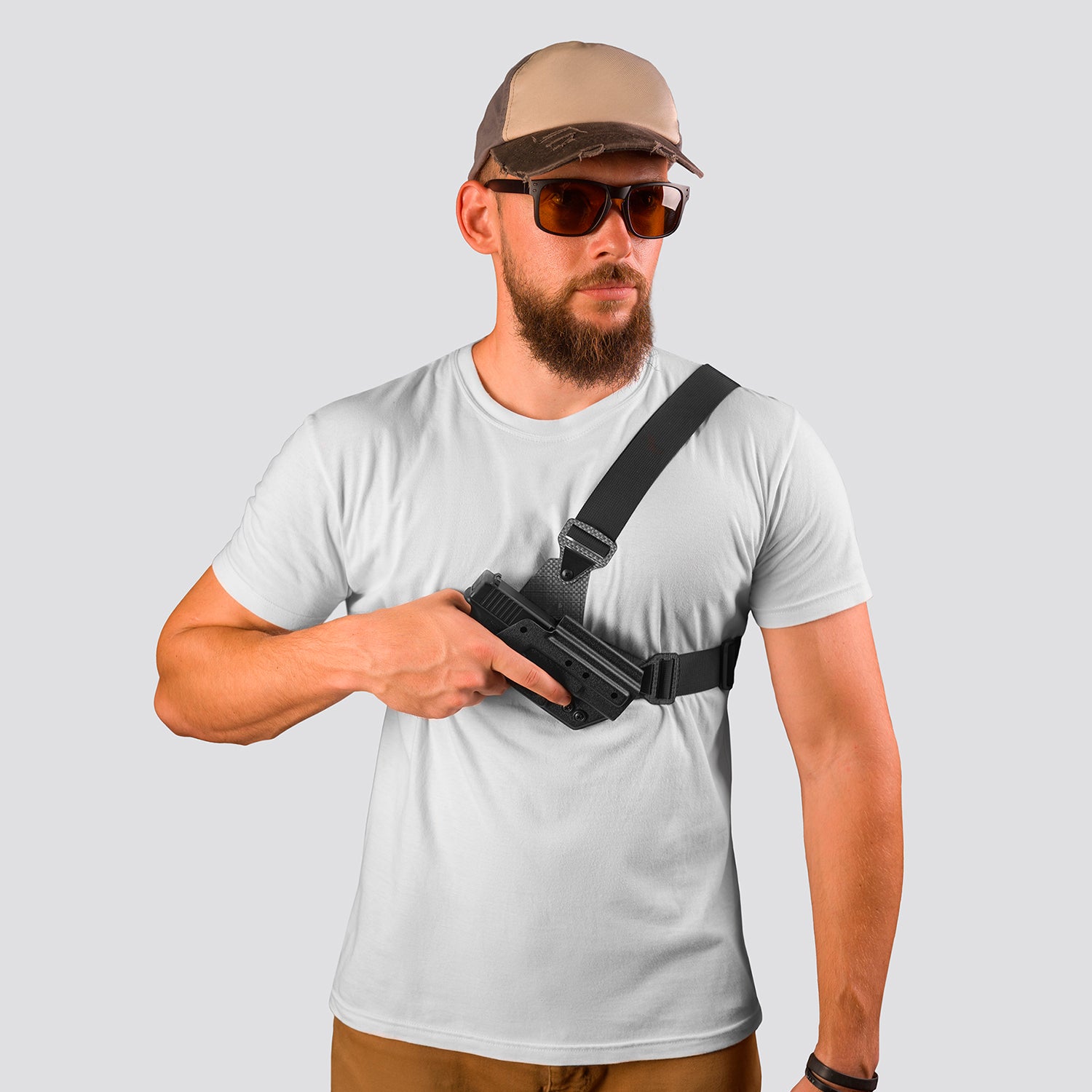 Man wearing a white t-shirt, beige cap, and sunglasses holding a black gun holster.