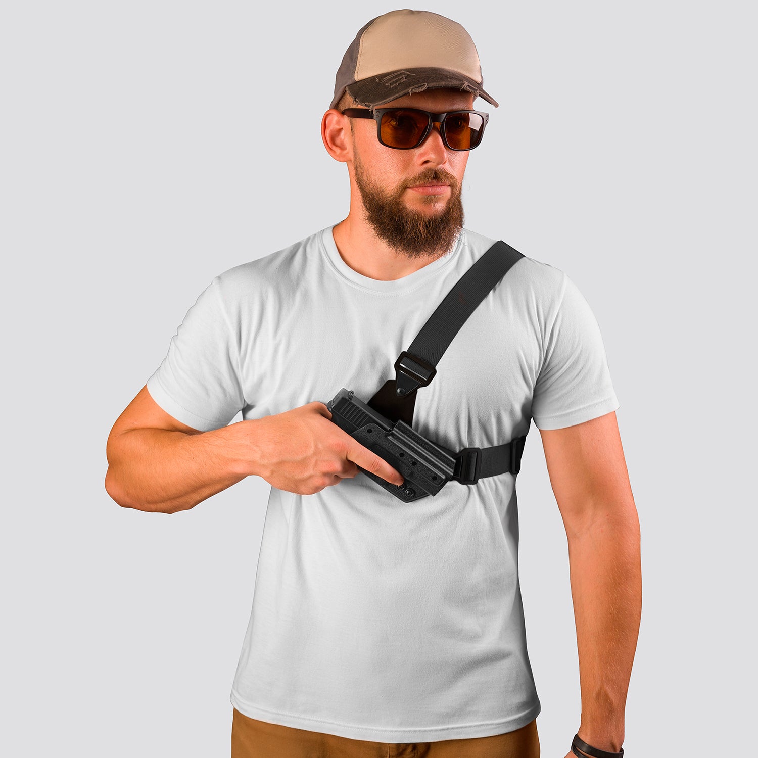 Man wearing a white t-shirt, beige cap, and sunglasses holding a gun holster.